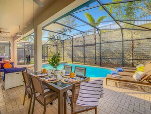 A sunlit patio with a pool, dining table, chairs, and lounge chairs. - EPIC! Themed-Arcade-Theatre-Pool Table-Pool&Spa-3mi>Disney (Kissimmee)