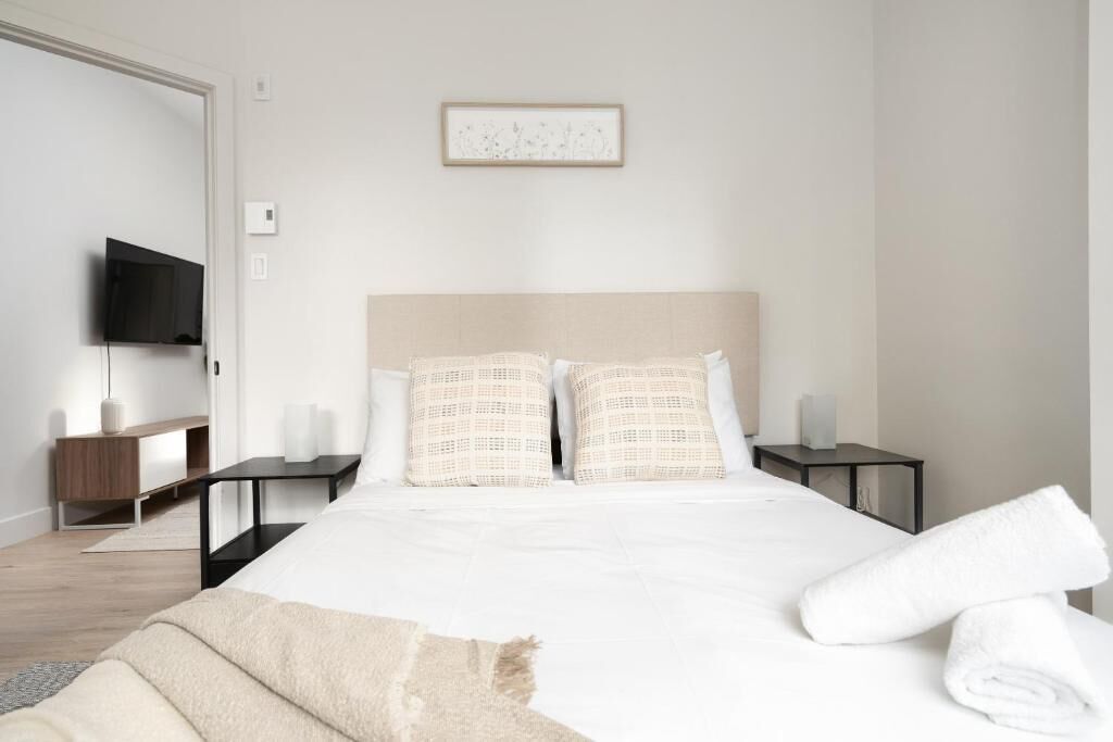 Hotellihuone, jossa on suuri sänky, kaksi yöpöytää, taulutelevisio ja seinällä oleva kehystetty taulu.