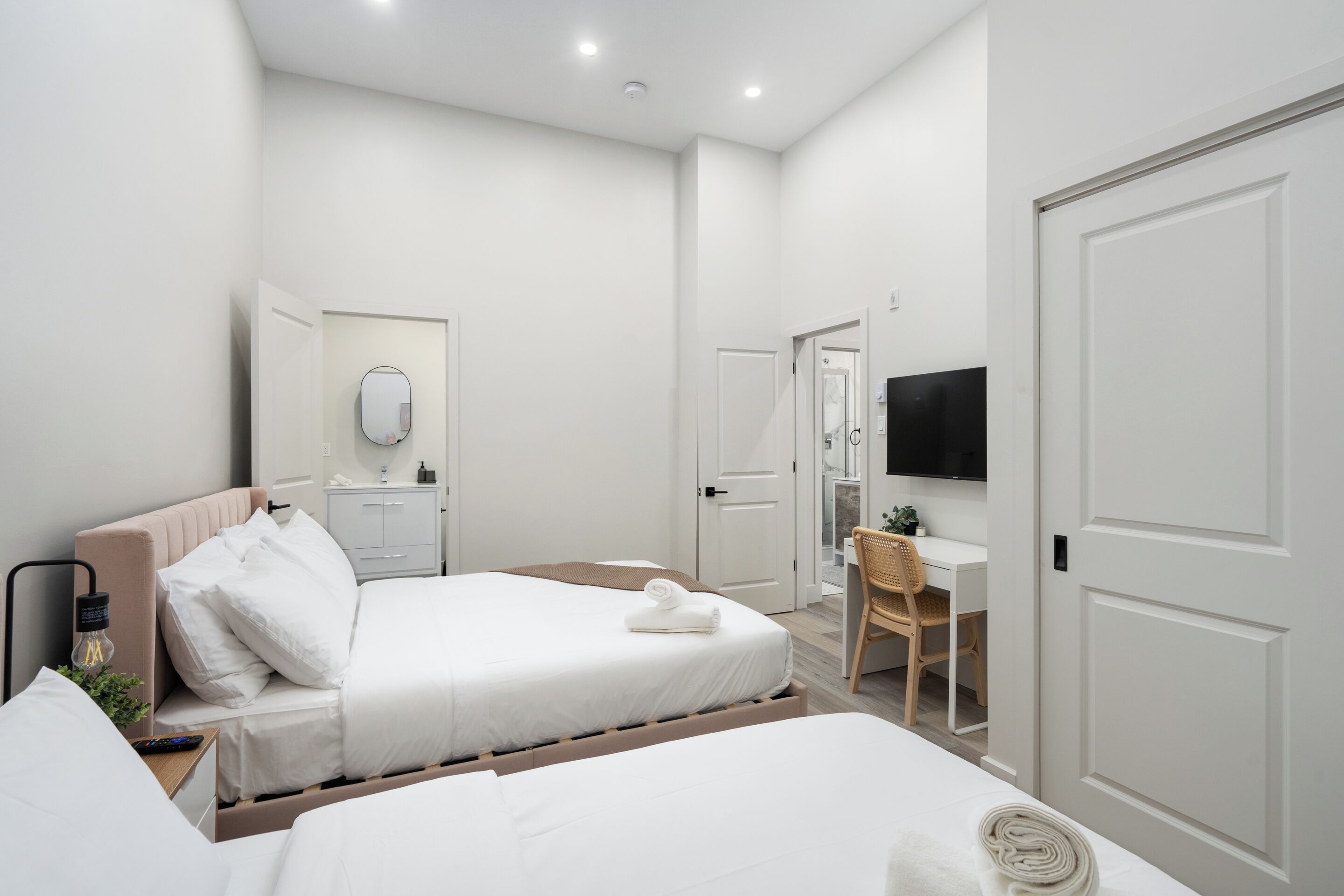 A hotel room with two beds, a desk, a chair, a TV, and a mirror.