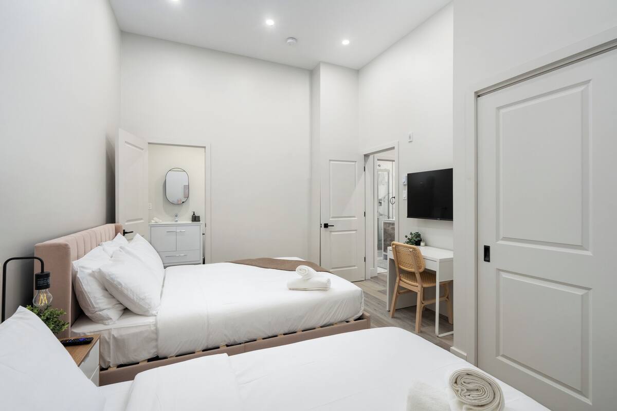 A hotel room with two beds, a desk, a chair, a TV, and a mirror.
