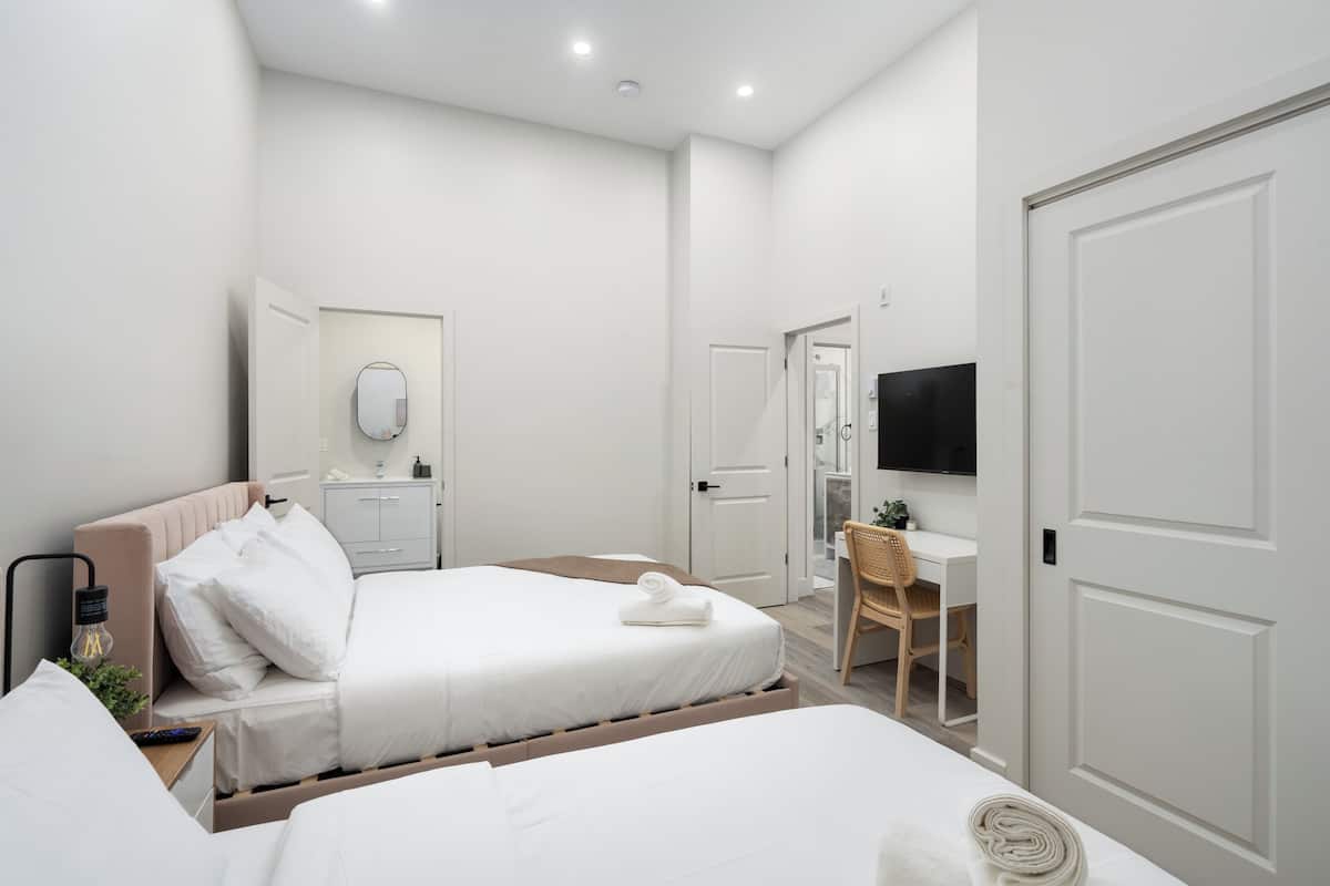 A hotel room with two beds, a desk, a chair, a TV, and a mirror.