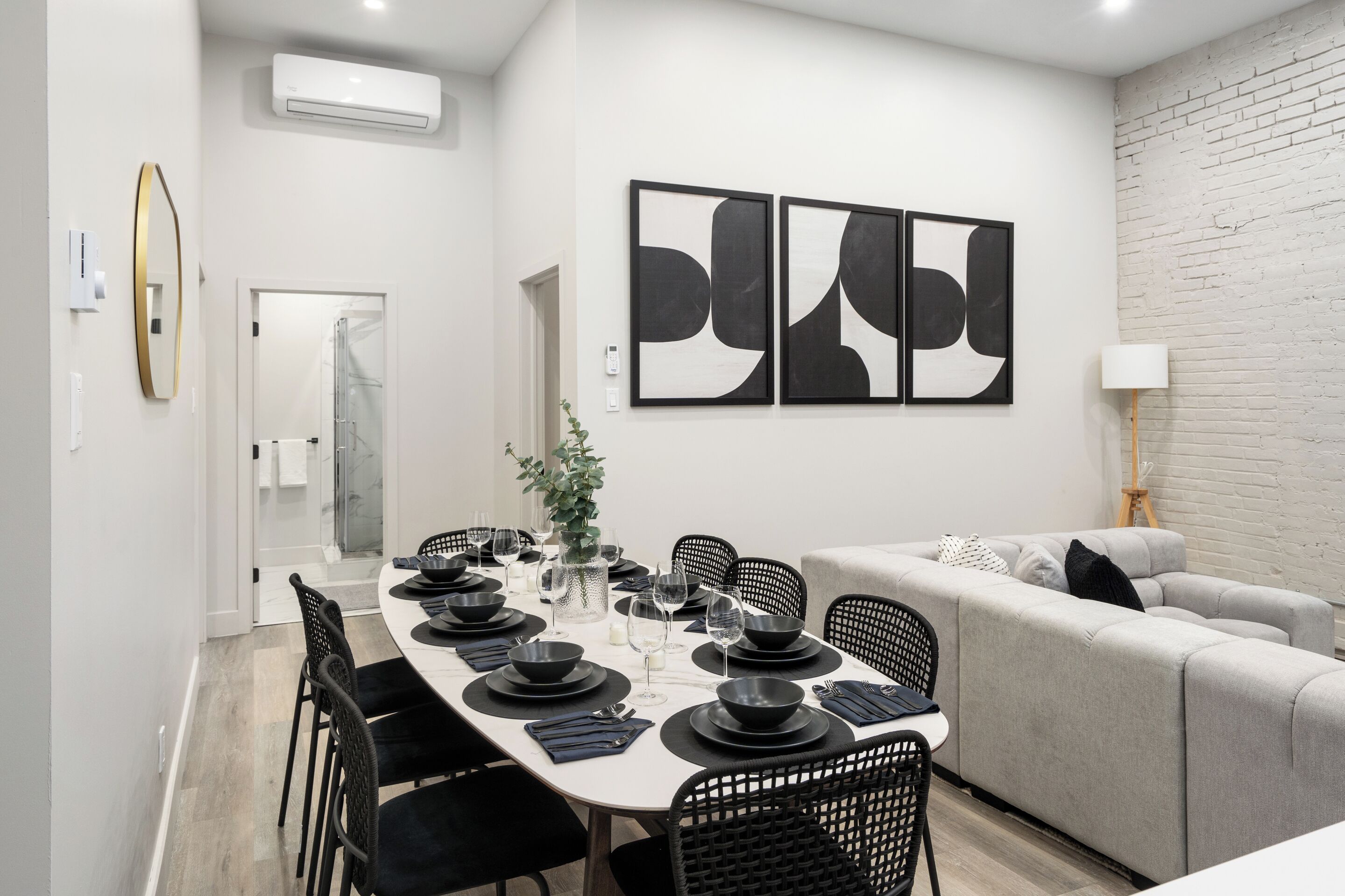 Un comedor moderno con una mesa blanca para seis, sillas negras y un sofá gris.