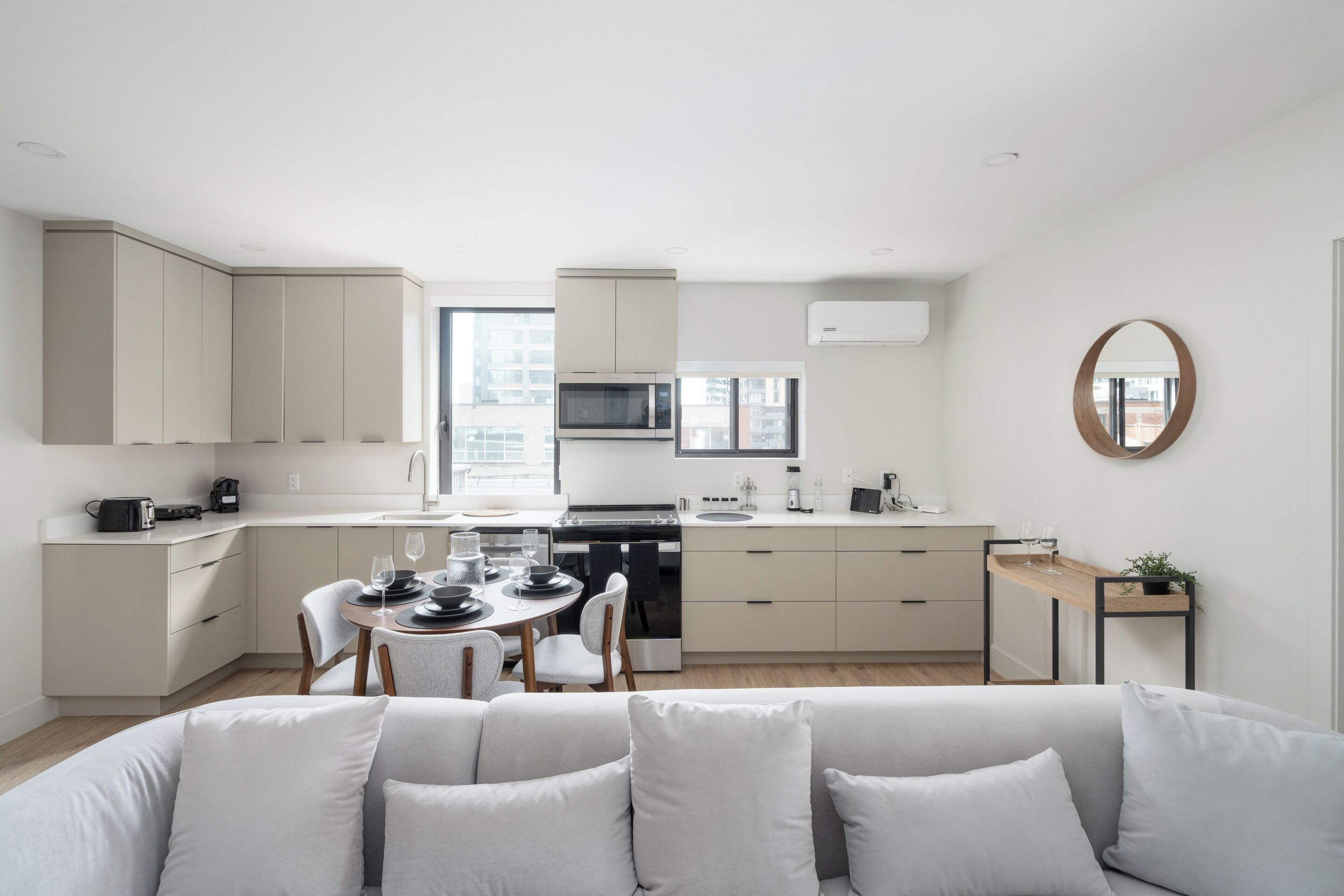 Une cuisine moderne avec des meubles blancs, un coin repas avec une table dressée pour deux personnes et un salon avec un canapé.