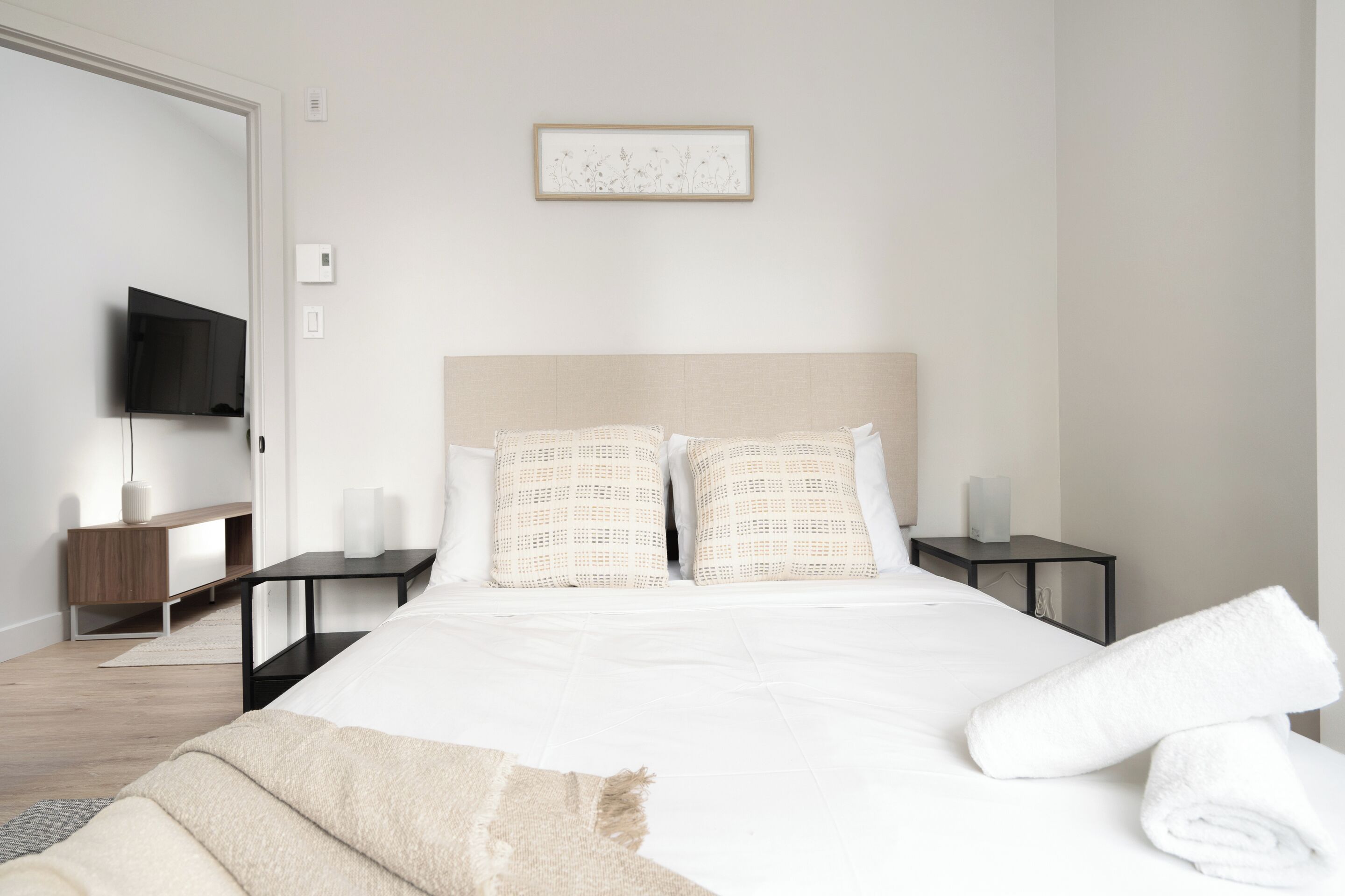 Une chambre d’hôtel bien rangée, avec un lit, un téléviseur à écran plat, des tables de chevet et un tableau encadré au mur.
