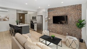A modern living room with a sofa, a coffee table, and a TV mounted on a brick wall. - The Griffin (Montréal)