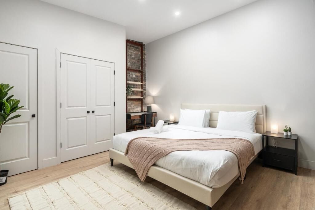 A bedroom with a large bed, white walls, a wooden floor, and a built-in shelving unit.