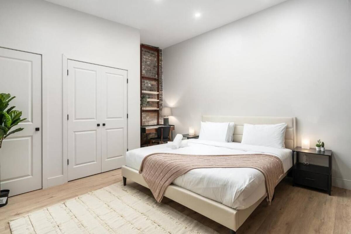A bedroom with a large bed, white walls, a wooden floor, and a built-in shelving unit.