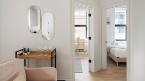 A modern room with a wooden table, two mirrors, a pink sofa, and a bed with a white headboard. - The Griffin (Montréal)
