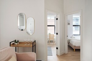 A modern room with a wooden table, two mirrors, a pink sofa, and a bed with a white headboard.