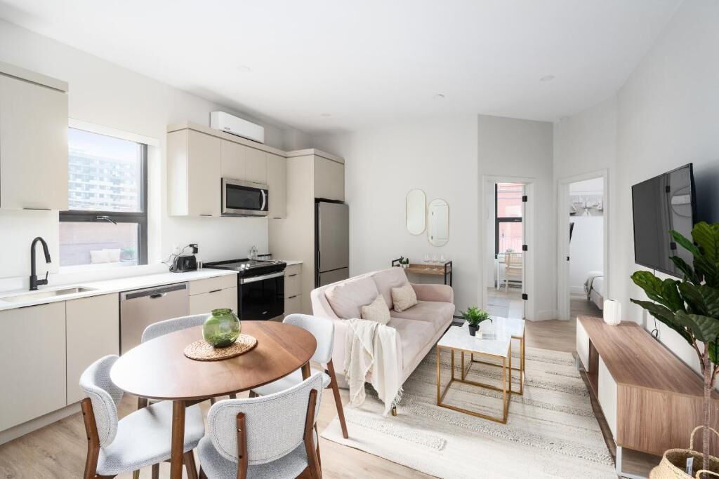 Una cocina moderna con armarios blancos, un microondas y un refrigerador. Hay una zona de comedor con una mesa y sillas de madera. Un sofá y una mesa de centro están en la sala de estar.