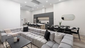 A modern living room with a sectional sofa, a dining area with a black table and chairs, and a kitchen in the background. - The Griffin (Montréal)