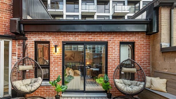 A brick building with a glass door entrance, two wicker chairs, and potted plants. - The Griffin (Montréal)