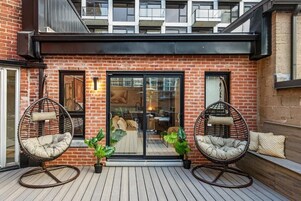 A brick building with a glass door entrance, two wicker chairs, and potted plants.