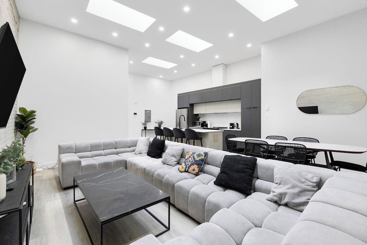 A modern living room with a grey sectional sofa, a black coffee table, and a dining area with a white table and black chairs.