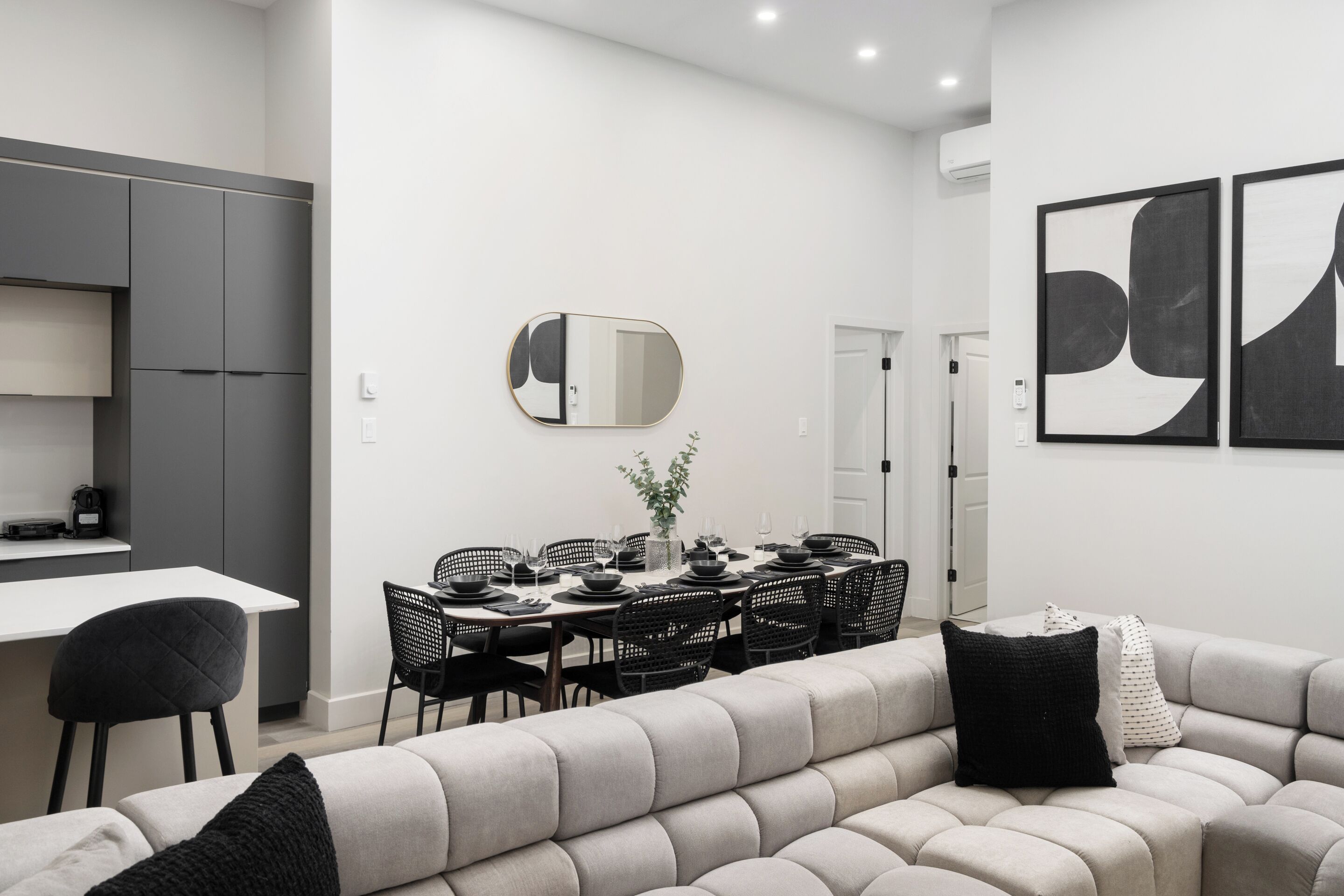 Une cuisine moderne avec des meubles gris, un coin repas avec une table ronde et des chaises, et un canapé gris agrémenté de coussins noirs.