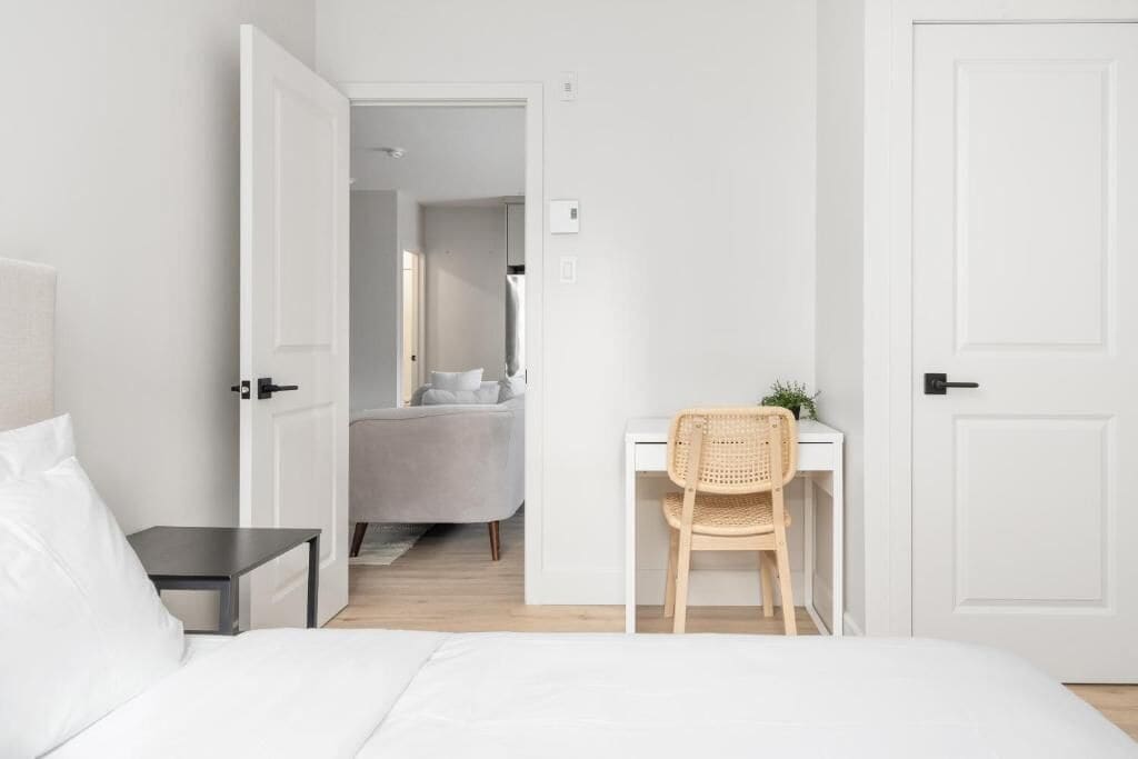 A bedroom with a bed, a desk, a chair, and a door leading to another room.
