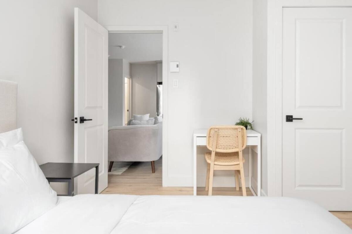 A bedroom with a bed, a desk, a chair, and a door leading to another room.