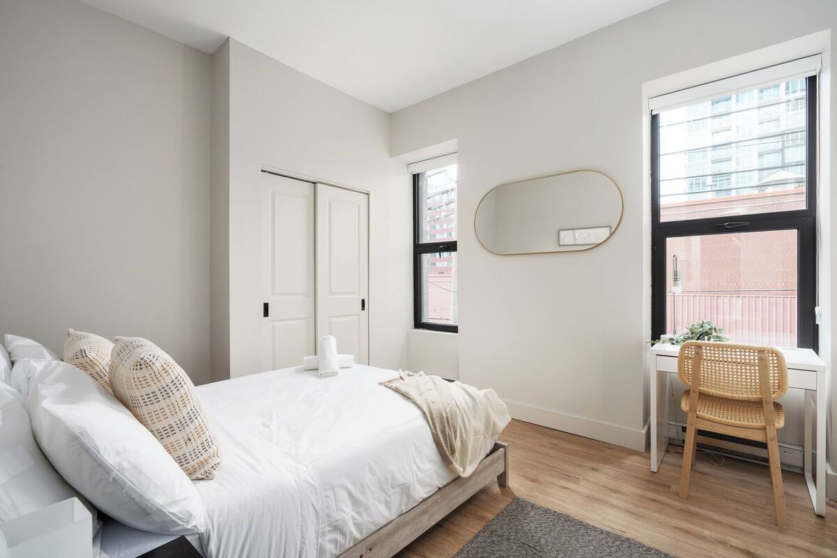 A bedroom with a bed, a desk, a chair, a window, and a door.