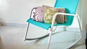 A teal rocking chair with cushions against a plain wall, a tiled floor, and two circular mirrors above. - THE WINDOW TO THE SEA (Alghero)