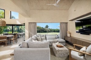 A spacious living room with a large sectional sofa, a stone coffee table, and a flat-screen TV mounted on the wall.