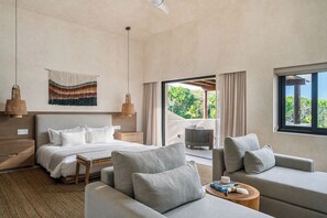 A hotel room with a bed, two sofas, a small table, a window with a view, and a door leading to an outdoor area.