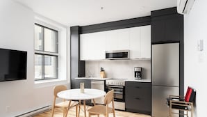 A modern kitchen with white and black cabinetry, a built-in microwave, a stainless steel refrigerator, and a dining area with a round table and wooden chairs.
