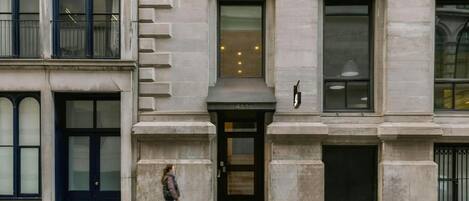 A building with a classical architectural style, featuring a prominent entrance with a black door, large windows, and a balcony with metal railings.