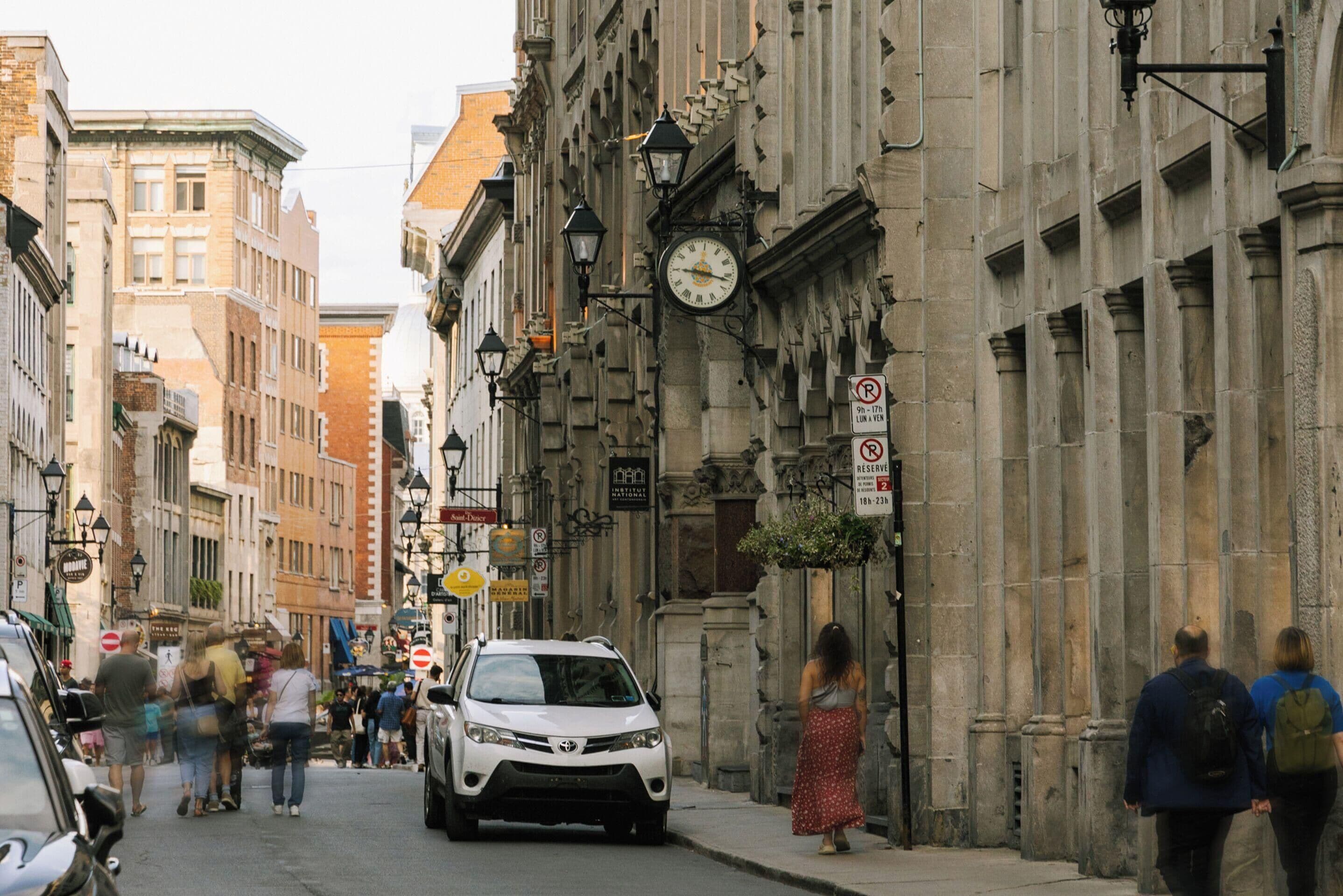 A street with buildings, a clock, and a car.
