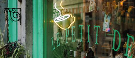 Una ventana de café con un letrero de neón, una puerta verde y varios objetos a la vista en el interior.