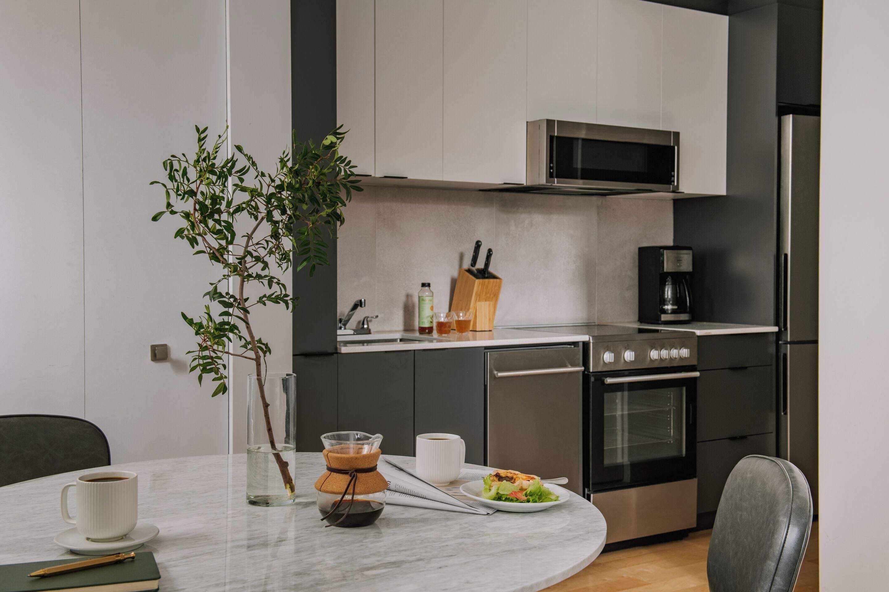 Una cocina moderna con microondas, estufa y lavavajillas. Hay una mesa de comedor con una taza, un libro y una planta.