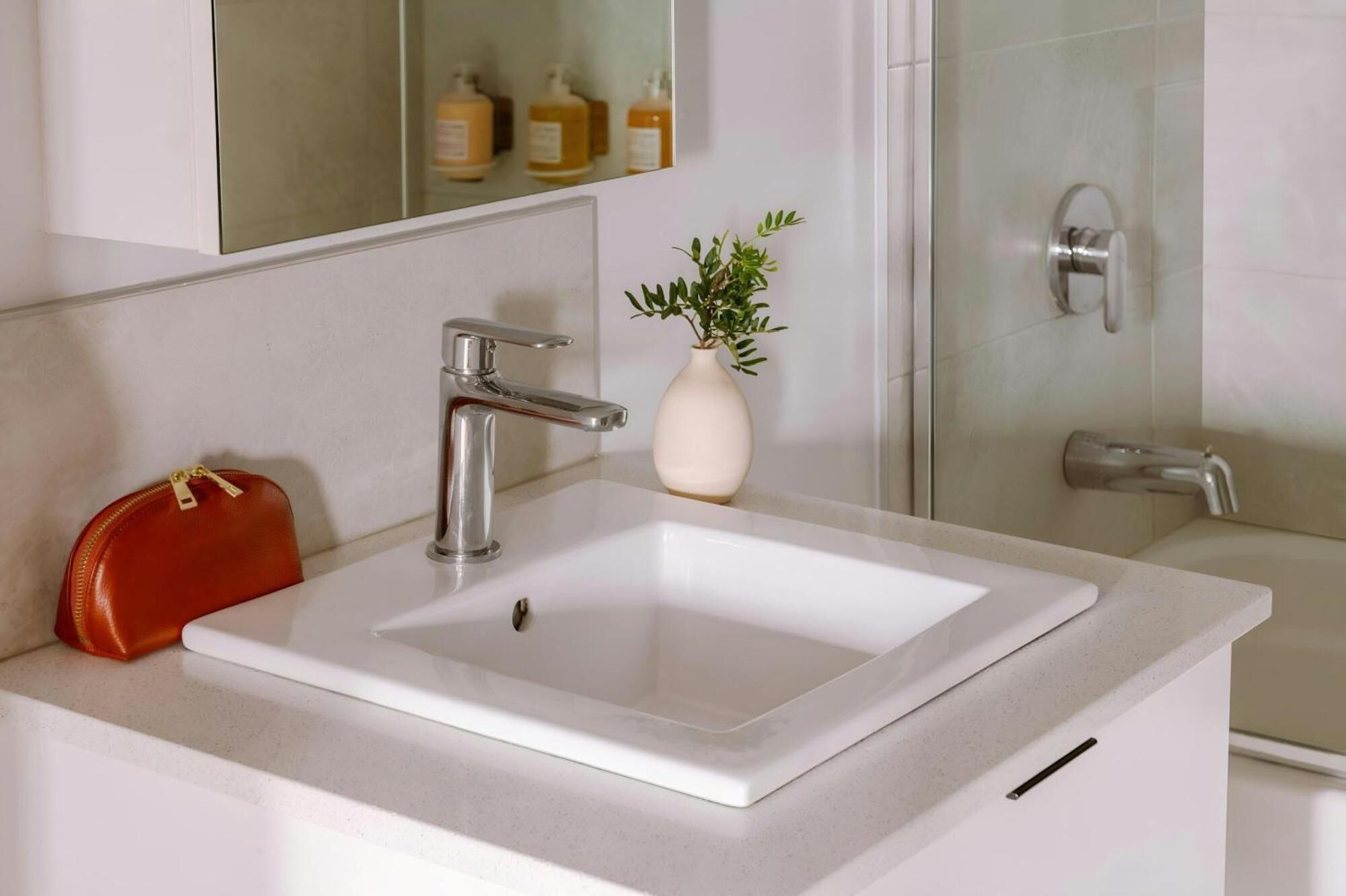 A bathroom with a white sink, a red handbag, a potted plant, and a glass shower enclosure.