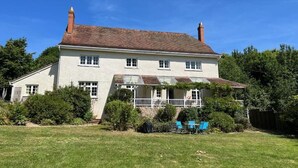 A two-story house with a white exterior, a tiled roof, and a small porch with blue chairs. - Croydon House (Minehead)