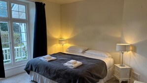 A bedroom with a bed, two bedside lamps, a window with curtains, and a radiator. - Croydon House (Minehead)