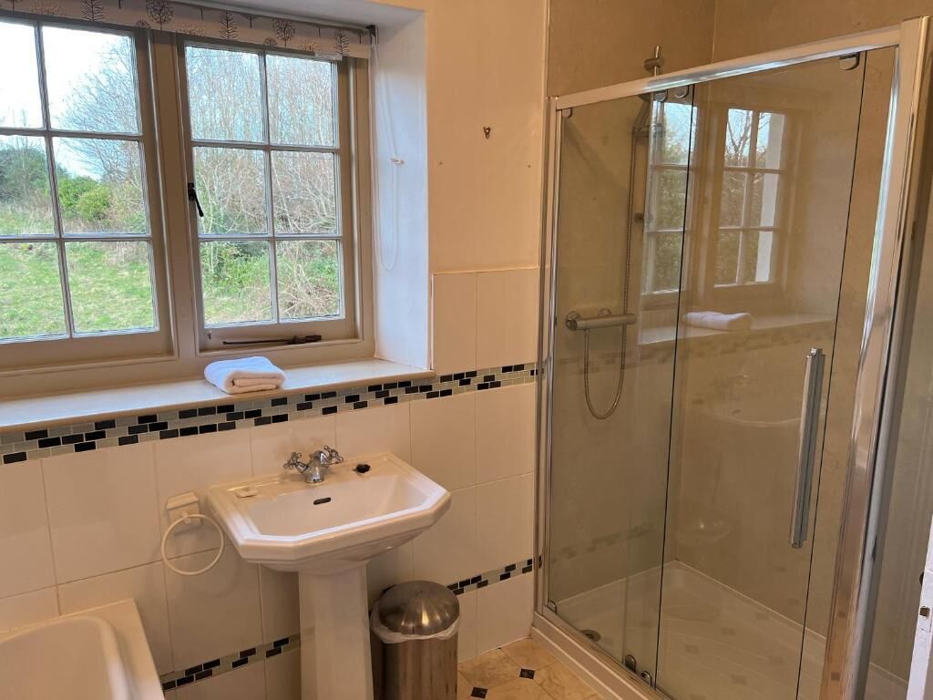 Et badeværelse med et vindue, en vask, et toilet og en brusekabine med glasvægge.