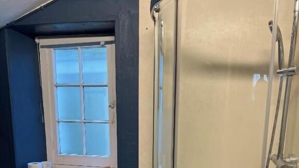 A bathroom with a glass-enclosed shower, a window with a view, and a small shelf with towels and toilet paper. - Croydon House (Minehead)