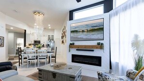 Ein modernes Wohnzimmer mit Kamin, Essbereich und einer Küche im Hintergrund.