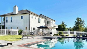 Ett tvåvåningshus med en swimmingpool, en täckt uteplats och ett vitt staket.