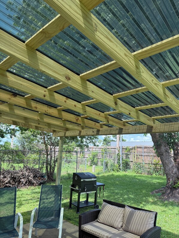 A covered patio area with a grill, chairs, and a sofa.