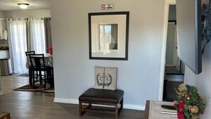 A modern living room with a dark brown bench, a framed picture above it, and a decorative plant on a table. - A Home for guests on Budget. (Broken Arrow)
