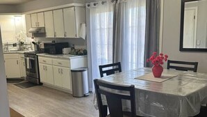 A modern kitchen with white cabinets, a stainless steel range hood, and a dining area with a table and chairs. - A Home for guests on Budget. (Broken Arrow)