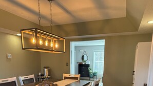 Een eetruimte met een lange tafel, witte stoelen en een hanglamp.