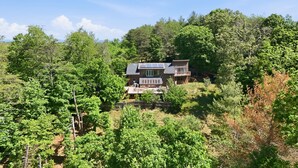 A two-story house with a balcony, surrounded by dense forest. - Blue Mountain Retreat | Sunset Views | Fire Pit (Alexander)
