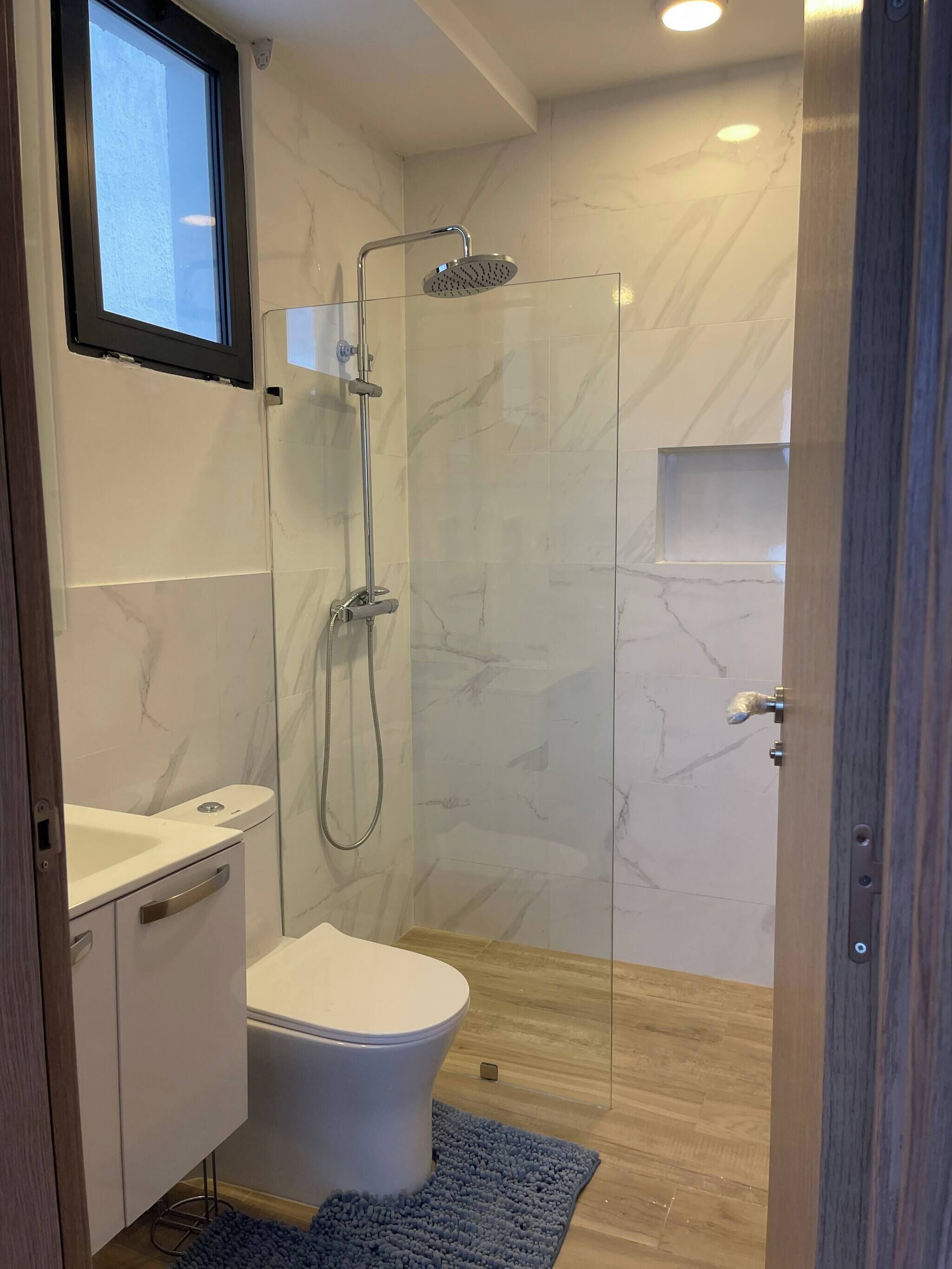 Un baño moderno con cabina de ducha de vidrio, inodoro blanco y tocador con lavamanos.