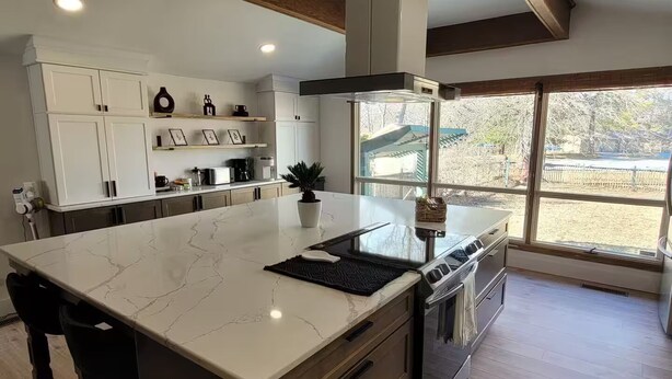 Cozinha moderna com uma ilha grande, armários brancos e vista para o exterior.