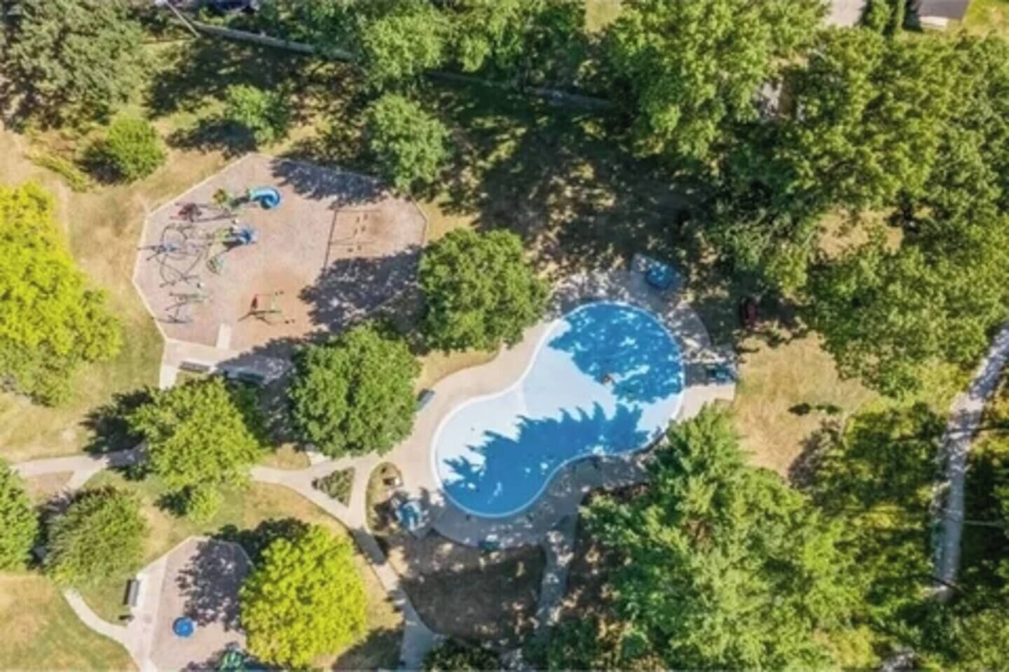 Vue aérienne d’un quartier résidentiel avec une piscine entourée d’arbres.