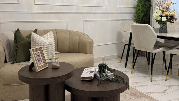 A modern living room with a beige sofa, two round wooden side tables, a dining area with a white table and chairs, and a large window with curtains. - Elegant boutique apartment 7 minutes away from the beach | Bayahibe  (Bayahíbe)