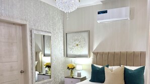 A bedroom with a bed, a nightstand, a mirror, a chandelier, and an air conditioning unit. - Elegant boutique apartment 7 minutes away from the beach | Bayahibe  (Bayahíbe)