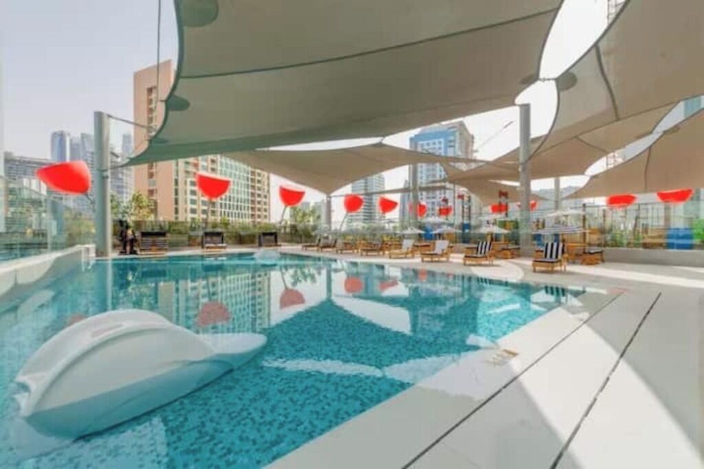 A swimming pool with lounge chairs and umbrellas, surrounded by high-rise buildings.