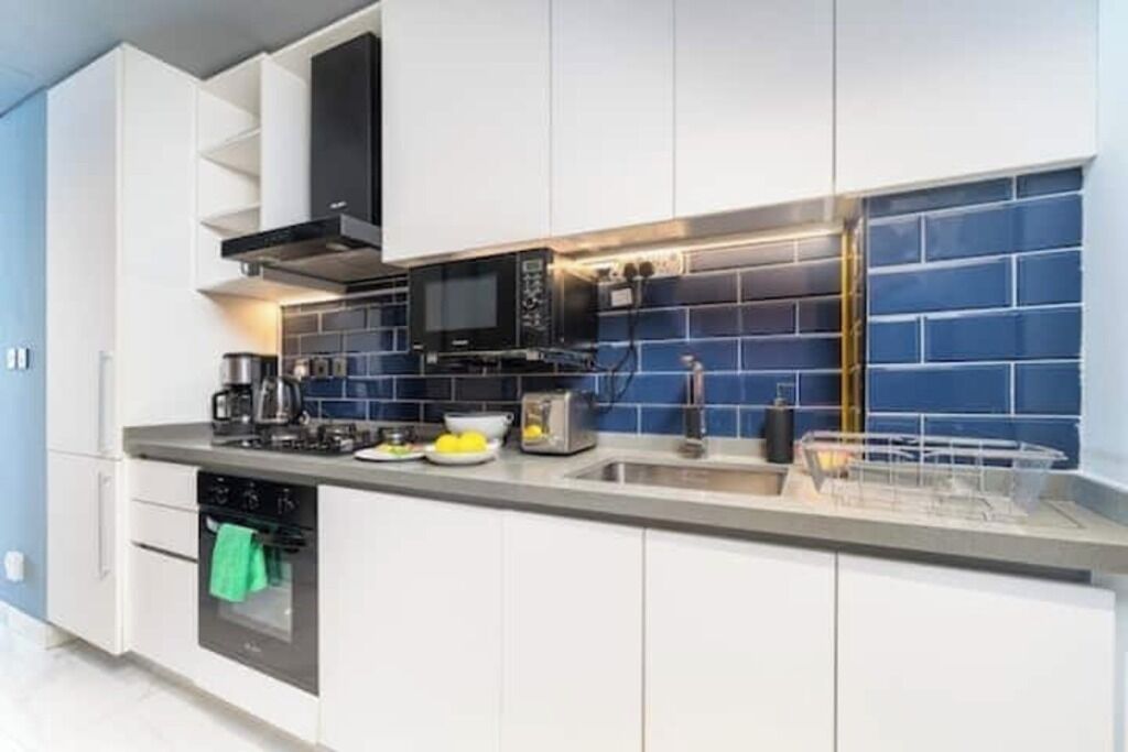 A modern kitchen with white cabinets, a black microwave, and a blue-tiled backsplash.