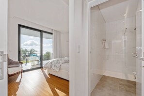 A modern bedroom with a large sliding glass door leading to a balcony, a separate shower area, and a wooden floor. - Atlantic Bloom by Homie (Funchal)